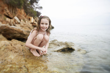 Full length of cute girl crouching on rock by sea