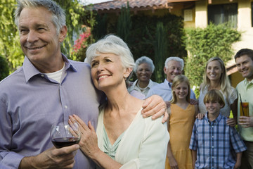Happy senior couple standing together with family and friends in the background