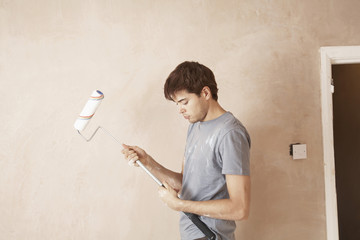 Side view of man assembling paint roller in unrenovated room