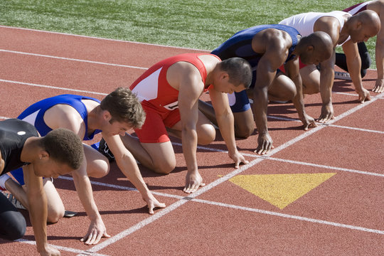 Group of multiethnic male runners at starting blocks in racetrack