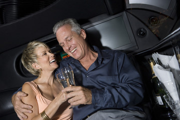 Happy mature couple toasting champagne sitting in limousine and toasting - obrazy, fototapety, plakaty