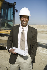 Portrait of a happy male architect holding blueprint at construction site