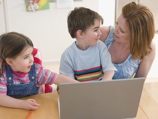 Young woman and children with laptop sitting at table in house