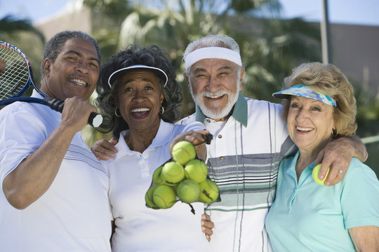 Portrait of happy senior friends with tennis balls and racquet in court