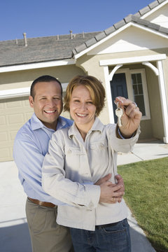 Portrait of happy mature couple holding key in front of new house