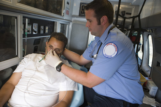 Male EMT professional helping man with oxygen mask inside ambulance