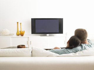 Rear view of young couple on sofa watching TV in living room