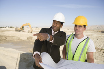 Architect and worker in discussion with blueprint at construction site