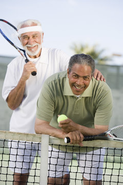 Portrait of happy senior male friends playing tennis