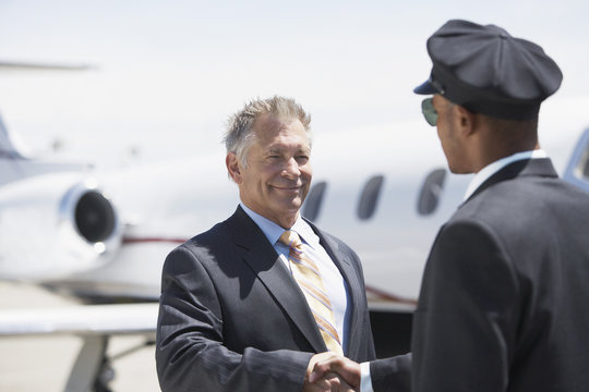 Smiling senior businessman shaking hands with pilot and blurred aircraft in the background - Powered by Adobe