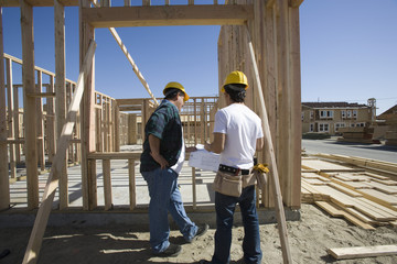 Male architects with blueprint constructing new wooden house