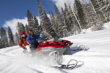 Couple driving snowmobile on snow covered track - obrazy, fototapety, plakaty