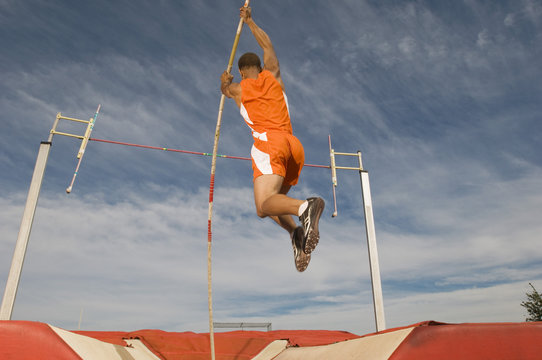 Male athlete pole vaulting against cloudy sky