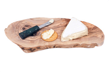 Supremely creamy soft ripened brie cheese with knife and cracker on olive wood cutting board isolated on white background