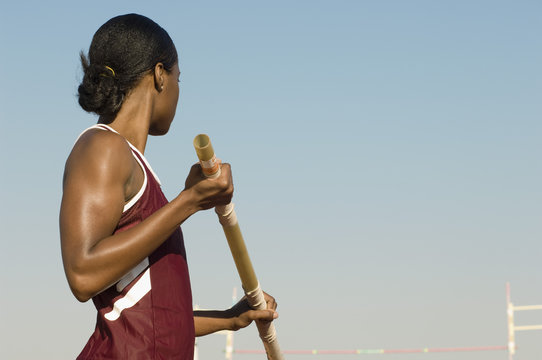 African American female pole vaulter holding pole against clear sky