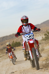 Female motocross rider riding motorbike with son in the background at track