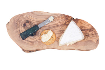 Supremely creamy soft ripened brie cheese with knife and cracker on olive wood cutting board isolated on white background
