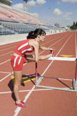 Full length of female athlete stretching leg before hurdle race