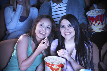 Young friends eating popcorn while watching film in movie theater