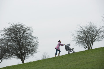 Full length of young mother pushing stroller uphill in park