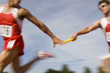 Blurred motion male runners passing baton in relay race - Powered by Adobe