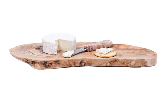 Soft ripened goat milk brie cheese with knife and pepper and poppy cracker on olive wood cutting board isolated on white background