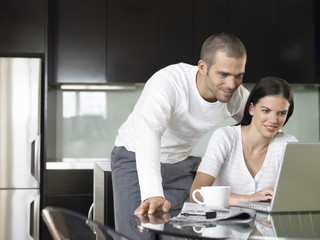 Happy young couple using laptop at dining table in modern kitchen