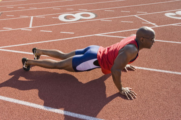 Full length of an African American male athlete makes pushups on a racetrack