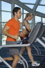 Fototapeta na wymiar Side view of man and woman on treadmill at gym