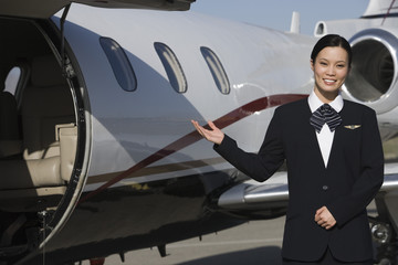 Portrait of a beautiful stewardess gesturing by airplane at airfield