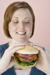 Happy beautiful woman looking at hamburger over pink background