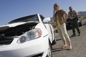 Tilt image of a woman having conversation on mobile phone with traffic cop writing ticket in the...