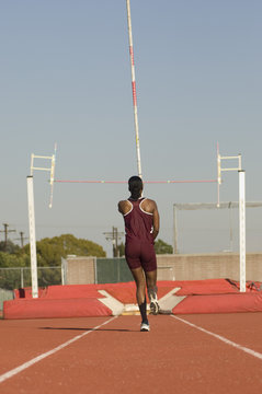 Rear view of female pole vaulter running with pole