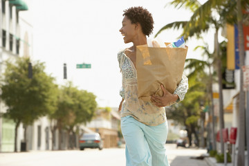Cheerful African American woman carrying grocery bag while walking on street
