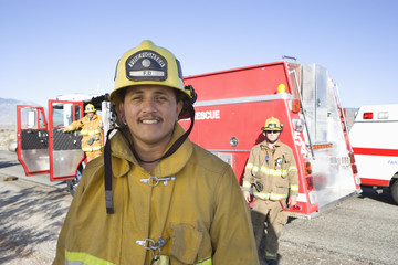 Portrait of a happy mature fire worker with coworkers in the background