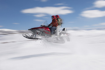 Side view of a couple jumping snowmobile in snow