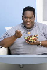 An African American obese man watching television while eating fruits at home