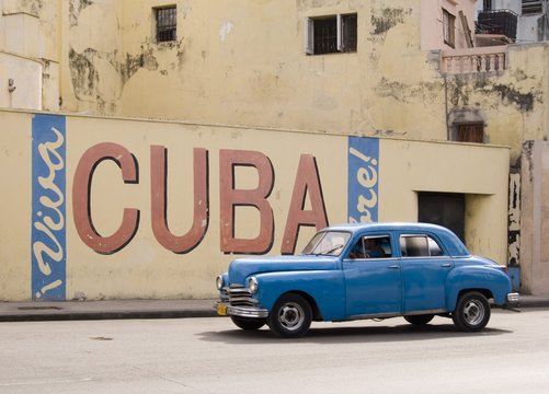 A vintage 1950's American car passing a 'Viva Cuba' sign painted on a wall in cental Havana, Cuba
