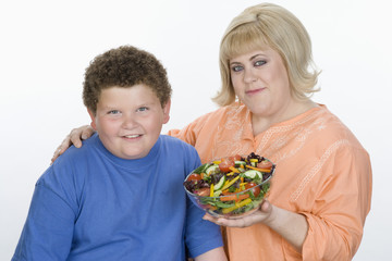 Portrait of mother and son holding bowl of salad isolated over white background