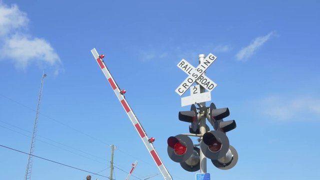 CLOSE UP: Railroad crossing sign with red lights flashing and barriers lowering