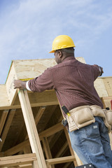 Rear view of male worker measuring a wooden beam at construction site