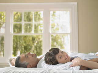 Portrait of happy woman lying with husband in bed