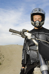 Portrait of male off road motor bike rider with motor bike at racing track against sky