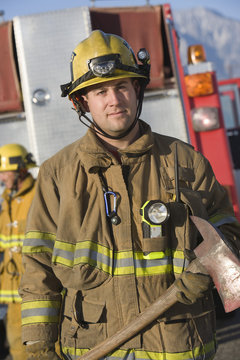 Portrait of a middle aged male firefighter holding axe with man in the background