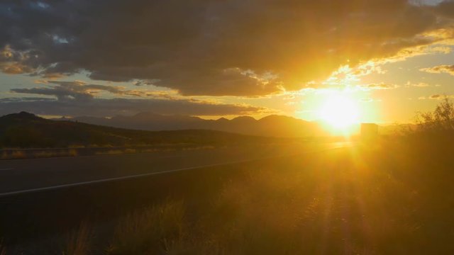 Freight semi truck speeding on empty highway over golden sun at summer sunset