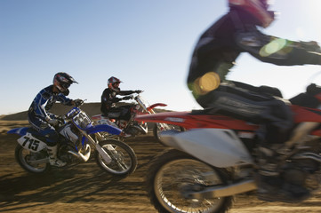 Three motocross racers racing in desert against blue sky