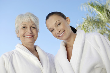 Portrait of two multiethnic women in bathrobes against blue sky at spa