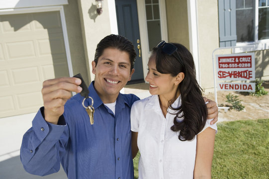 Portrait of Hispanic man with arm around woman holding keys of their new house