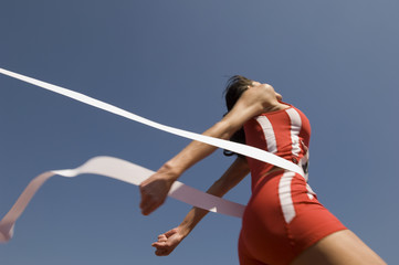 Low angle view of young female athlete crossing finish line against clear blue sky - Powered by Adobe