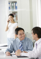 Two business colleagues in discussion with woman using cellphone in the background